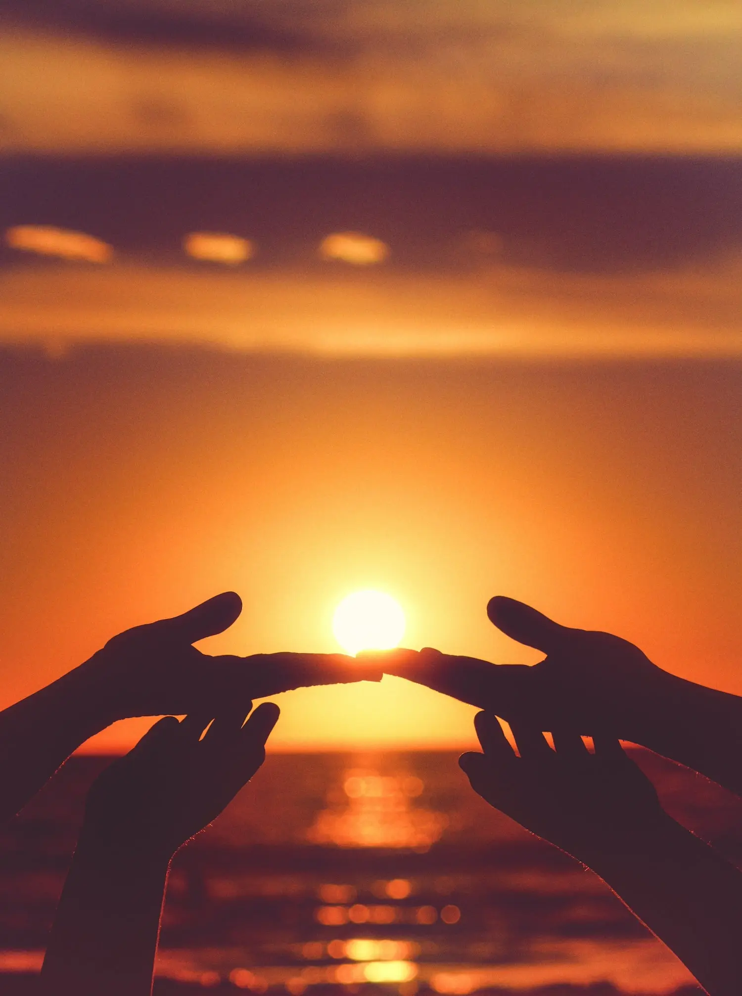 Silhouette der Hände, die hochgestreckt sind und sich während des Sonnenuntergangs berühren